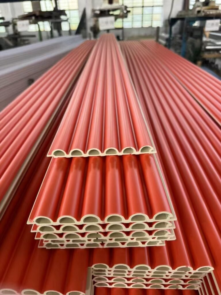 Vibrant orange-red WPC semi-circle wave panels stacked in factory, showcasing mass production and bulk supply of safe, rounded fluted wall cladding for vibrant interior designs.